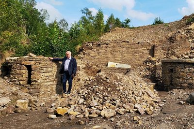 Reste des alten Freibads. Frank Riedel steht vor der Säule, die zusammen mit der Mauer im Hintergrund und dem Nixen-Podest erhalten werden sollen. Die Säule rechts wird wieder unter Erdmassen verschwinden. 