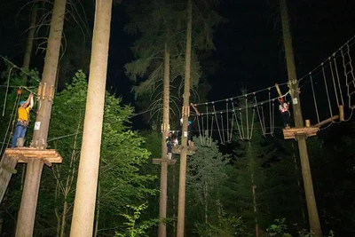 Das Meistern der verschiedenen Elemente des Kletterwalds ist im Dunklen weitaus schwieriger als bei Tageslicht. Ohne das Blitzlicht des Fotografen wären die Kletterer nur zu erahnen.
