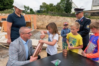 Oberbürgermeister André Heinrich hilft Maida aus der zweiten Klasse der Lauterbacher Grundschule beim Befüllen der Zeitkapsel. 