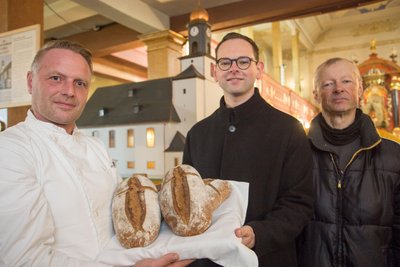 Bäckermeister Marcel Kolar sowie Tobias Haueis und Bert Körner vom Ausschuss (v. l.) mit dem Spendenbrot. Ein Teil des Erlöses soll in die Sanierungsarbeiten des Zöblitzer Kirchturms investiert werden.