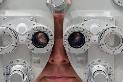 Ein Mann sitzt hinter einem sogenannten Phoropter, mit dem die Sehstärke eines Patienten bestimmt werden kann.