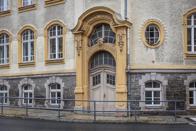 Errichtet in den Jahren zwischen 1907 und 1909 ist über der Tür heute noch der Schriftzug „Ohne Fleiß kein Preis“ zu lesen. Der Fassadenschmuck ist der Posamenten-Ornamentik entnommen.