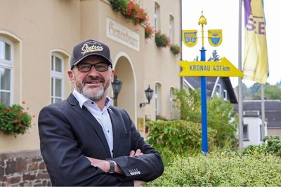Lutz Rosenlöcher vor dem Rathaus. Der Wegweiser rechts gibt die Entfernung in die Partnergemeinde in Baden-Württemberg an.