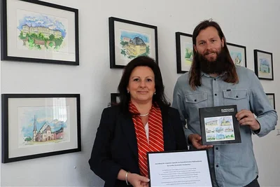 Kerstin Mayer von der Sparkasse und Nick Pfeifer-Mühlbach von der Wirtschaftsförderung in der Ausstellung mit den Original-Aquarellen, die den Stadtrundgang durch Crimmitschau begleiten.