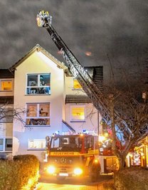 Feuerwehrleute kontrollieren den Schornstein auf dem Mehrfamilienhaus in Seifersdorf mit Hilfe einer Drehleiter.