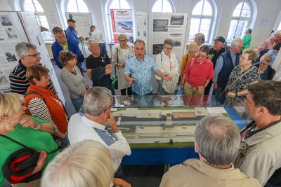 Organisator Andreas Hütter (Mitte im blauen Hemd) erläutert ein Modell des Chemnitzer Flughafens in der Ausstellung anlässlich des 100-jährigen Jubiläums.