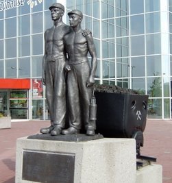Die Plastik "Alter und junger Bergmann" steht beim Glück-Auf-Center vor einem Möbelhaus.