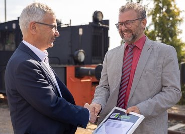 Auszeichnung vor einem ausgedienten Reisezugwagen, der in Neumark künftig der Ausbildung dient. Landrat Rolf Keil (links) beglückwünscht Schulleiter Sven Müller vom Johann-Heinrich-Pestalozzi-Gymnasium für das Engagement der Schule bei der Woche der offenen Unternehmen. 