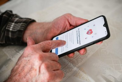 Ein Senior hält ein Smartphone in den Händen und versucht einen Termin beim Hausarzt zu buchen.