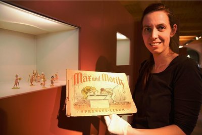 Museumsleiterin Tina Reitz zeigt ein historisches Sammelbilder-Album zu Max und Moritz. Es ist in der Sonderausstellung über Wilhelm Busch zu sehen. 