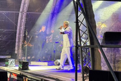 Sänger Dirk Wölfl war in weißem Anzug gekleidet. Im Hintergrund: der Dirigent und die Musiker des Karlsbader Sinfonieorchesters.