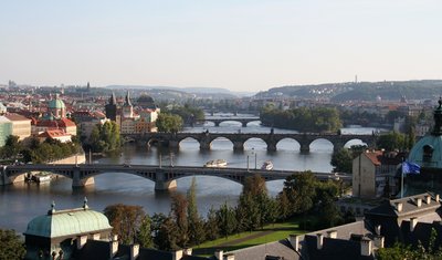 Der Fluss, dem eine der berühmtesten Sinfonische Dichtungen der Musikgeschichte gewidmet ist: Die Moldau, hier im Bereich zwischen Prager Altstadt und Kleinseite. Das sinfonische Werk endet mit dem Vysehrad-Motiv. Der darin besungene Burgwall liegt im Südwesten auf einem Felsen hoch über dem Fluss, der daran vorbeifließt, kurz bevor er das Zentrum durchquert. Die  linke Uferstraße im Bildbereich ist nach Friedrich Smetana benannt, hinter der von Statuen gesäumten Karlsbrücke hat das Smetana-Museum seinen Sitz.
