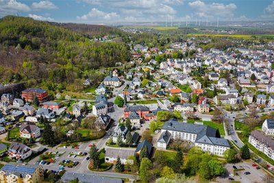 Ein aktuelle Luftansicht von Oelsnitz mit markanten Gebäuden wie Roter Schule, Rathaus, Kirche und Stadthalle.