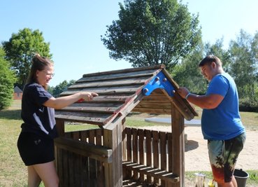 Die 17-jährige Helene Gläser und der 19-jährige Lucas Pursche schleifen und kratzen als freiwillige Helfer gemeinsam alte Farbe von einem Häuschen auf dem Spielplatz in Lößnitz. 