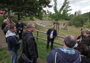 Auf dem Gelände des 2013 durch die Flut zerstörten Sportplatzes ist ein Amphitheater entstanden. In der Bildmitte Ortsvorsteher Lutz Weißpflug bei seinem Vortrag vor der Kommission. 