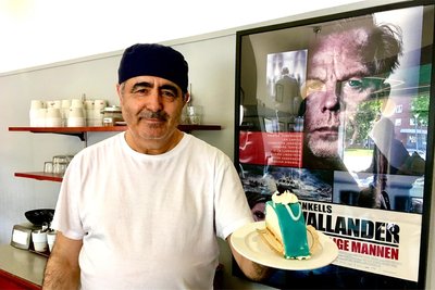 Hédi Chermiti, der Chef von Fridolfs Konditorei im schwedischen Ystad, mit einem Stück Wallander-Torte. Die blau gefärbte Marzipanschicht soll an die Polizeiuniform erinnern, Schlagsahne, Vanillecreme und Punsch runden das Ganze ab. Auch Kurt-Wallander-Darsteller Krister Henriksson mag die Torte.