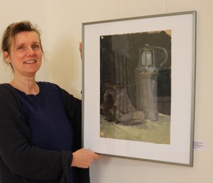 Galerie-Mitarbeiterin Daniela Kolbe mit dem Bergbaustillleben von Karlheinz Walther, auf dem er 1958 seine später verschwundene Grubenlampe neben einem Schuh aus dem Schulfundus im Unterricht gemalt hat. 