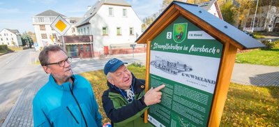 Der stellvertretende Bürgermeister Dieter Herold (links) und Christian Sehm, Vorsitzender des Heimatvereins Auerbach, die an einer der Geschichtstafeln an insgesamt sieben ehemaligen Strumpffabriken im erzgebirgischen Auerbach stehen. 