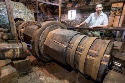 Museumsleiter Lasse Eggers steht hinter der rund 9,5 Meter langen Welle, die die drei Hämmer antreibt und die erneuert werden muss.