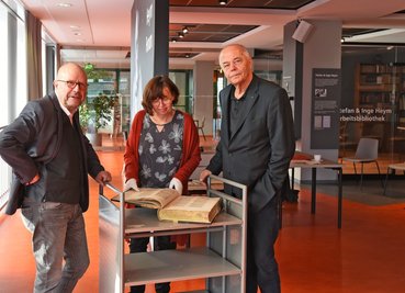 Stefan Tschök, Anja Schrön und Curt Bertram (von links), Vorstandsmitglieder der Förderer der Stadtbibliothek, begutachten einen dank Spenden restaurierten Druck aus dem Chemnitzer Franziskanerkonvent von 1475. 