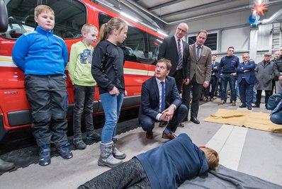 Im Gerätehaus der Freiwilligen Feuerwehr Kühnhaide ließ sich Ministerpräsident Michael Kretschmer (4.v.l.) von Nomi Lorenz (3.v.l.) von der Jugendfeuerwehr zeigen, wie die stabile Seitenlage funktioniert.