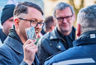 Vor der Demonstration hatte Tom Rodig den Polizisten den Hakenkreuz-Sticker gezeigt. Die Beamten verboten das Verteilen. Als der Aufkleber nach der Demo als Satireaktion übergeben wurde, griff die Polizei ein. 