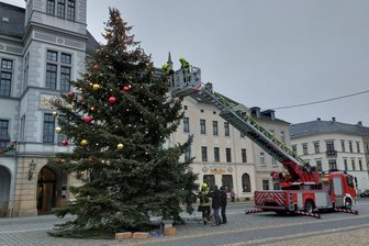 Abgeschmückt: Oelsnitz entfernt Weihnachtskugeln und sperrt Marktplatz - Die Freiwillige Feuerwehr Oelsnitz schmückt von der Drehleiter aus den Weihnachtsbaum vor dem Rathaus ab.
