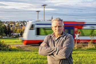 Ärger um den Ausbau der Citybahn bei Niederwürschnitz - Jörg Grimm steht vor seinem Feld, über das bald eine riesige Brücke führen soll. Hinter ihm fährt die 523 von Stollberg nach Glauchau.