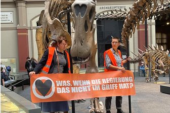 Aktivistinnen kleben sich an Dinosaurier im Berliner Naturkundemuseum fest - Zwei Klimaaktivistinnen mit einem Banner "Was, wenn die Regierung das nicht im Griff hat?" haben sich im Berliner Museum für Naturkunde an den Haltestangen eines Dinosauriers festgeklebt.
