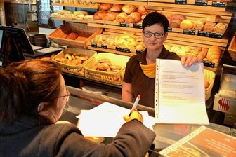 "Alarmstufe Brot" im Vogtland: Wie Kunden ihren Bäcker unterstützen - Nicht nur in der Tannenbergsthaler Bäckerei von Innungsobermeister Jörg Schürer werden Unterschriften für die Petition "Alarmstufe Brot" der sächsischen Handwerksbäcker gesammelt, die Verkäuferin Michaela Thoß einer Kundin über die Ladentheke reicht.