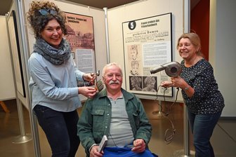 Als die Oederaner gemeinsam nackt badeten: Neue Schau zeigt 500 Jahre Arbeit der Bader - Ausstellungsaufbau macht Spaß: Andreas Seltmann wird von Sonja Voigt (r.) und Michaela Kruse symbolisch frisiert. Ein Dutzend Ausstellungstafeln stellen das Können und den Werdegang einer Zunft und ihrer Dienstleistungen vor.