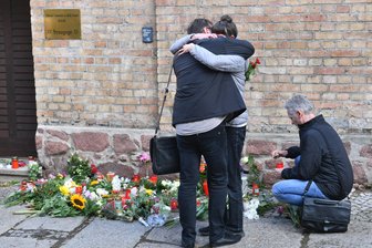 Menschen trauern vor Kerzen und Blumen an der Synagoge.