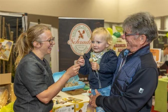 Auerbacher Gesundheitsmesse: Besucher erfahren, wie Telemedizin beim Mangel an Augenärzten helfen kann - Isabel Bolz von der Auerbacher Bäckerei Schrader gibt dem Zweijährigen Nick Leithold eine Kostprobe. Mit im Bild Klaus Bergert.