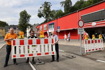 Auf der Bahnhofstraße in Schwarzenberg rollt der Verkehr wieder - Oberbürgermeister Ruben Gehart (l.) und Frank Kippig, der Geschäftsführer der Wasserwerke Westerzgebirge, heben zusammen mit Benjamin Rux (M.) von der VT-ERZ Verkehrstechnik die letzten Absperrzäune weg.