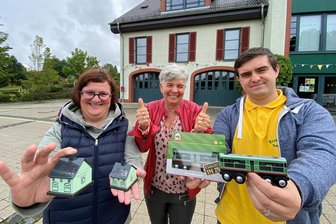 Auf diese Souvenirs fährt man jetzt schon ab: Der Bratwurschtgrund im Vogtland feiert am Wochenende 700 Jahre - Klein, aber oho. Diese Souvenirs gibt’s am Wochenende im Heinsdorfer Gemeindezentrum und im Lok-Schuppen nebenan. Antje Bochmann vom Landshop 24 mit dem ersten Heinsdorfer Räucherhäusel, Bürgermeisterin Marion Dick und Lukas Wolf vom Traditionsverein Rollbockbahn mit der ersten Rollbockbahn fürs Kinderzimmer.