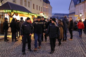 Auf Streife zwischen Waffeln und Wurst: Was die Polizei auf dem Schwarzenberger Weihnachtsmarkt erlebt - Streife laufen auf dem Schwarzenberger Weihnachtsmarkt: Bürgerpolizist Jens Kutzschke, Silvio Martin von der Sächsischen Sicherheitswacht und Polizistin Lenka Lehká aus Tschechien (v. l.) sind gemeinsam unterwegs.