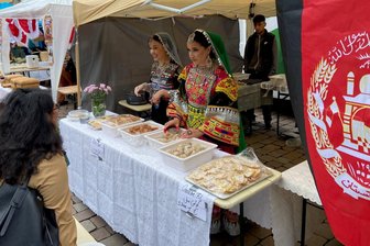 Auftakt Interkulturelle Wochen in Chemnitz: Die ganze Welt kocht auf dem Neumarkt - Am afghanischen Stand bieten Frauen in traditionellen Gewändern verschiedene Backwaren an.