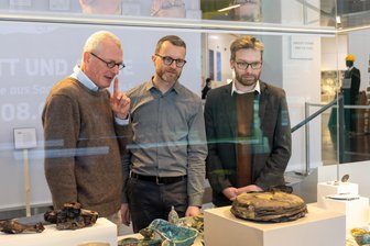 „Aus Schutt und Asche“: Archäologische Funde aus den Trümmern des Krieges – nicht nur in Chemnitz - Dr. Michael Strobel, Marcus Sonntag und Dr. Alexander Walther stehen an einer Vitrine mit Fundstücken aus Chemnitz und Dresden.