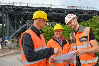 Außergewöhnlicher Schwertransport: Neue Göltzsch-Brücke im Vogtland angekommen - doch wie geht es jetzt weiter? - Hinter Mike Purfürst, Bürgermeister von Netzschkau, Ideengeber Georg Erdmann und Bauleiter Clemens Heinzig (von links) ist das Teilstück zu sehen, das in Chemnitz abgebaut wurde.
