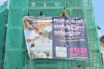 Azubi-Notstand im Handwerk: Wie ein Steinmetz aus Halsbrücke um Lehrlinge wirbt - Steinmetzmeister Tobias Neubert und Alireza Derakhsshani (l.) bringen das Werbebanner am Eckhaus Burgstraße/Kesselgasse an. 