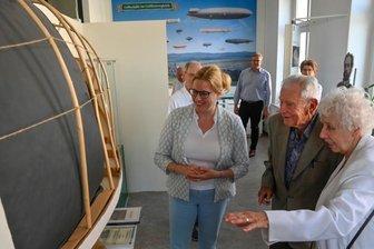 Baumgarten-Urenkelin besucht Grüna: Der "fliegende Oberförster", seine Nachfahren und eine lange Suche - Die Urenkel der wichtigsten deutschen Luftschiffpioniere des 19. Jahrhunderts treffen sich: Eva Weber (rechts), Nachfahrin von Georg Baumgarten, und Günter O. Schulz, Nachfahre von Hermann Wölfert, haben sich gemeinsam mit Silvia Slazenger, Tochter Eva Webers, die Gedenkausstellung in Grüna mit Luftschiffmodell angesehen.