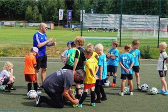 Binnen zwei Tagen ausgebucht: Warum ein Fußballcamp in Schöneck so beliebt ist - René Jahncke von Empor Berlin erläutert beim Schönecker Fußball-Camp den jüngsten Teilnehmern die nächsten Aufgaben. Er ist seit 2018 dabei. Werner Wilk vom VfB Schöneck kümmert sich derweil um die Schnürsenkel der Jüngsten.