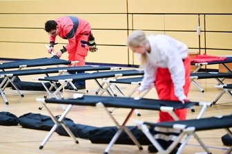 Blackout-Gefahr auch in Sachsen: „Es darf nicht vom Wohnort abhängen, ob Menschen so ein Ereignis überstehen oder nicht“ - Ehrenamtliche Rotkreuz-Mitarbeiter bauen im Südwesten Berlins in einer Notunterkunft Feldbetten auf.