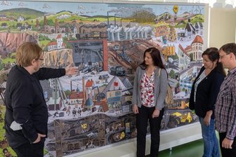 Blick in Sachsens Unterwelten: Schätze und Gefahr aus der Tiefe - Teil der Ausstellung ist ein großes Wimmelbild zu Sachsens Bergbaugeschichte. Hier erklärt Alexander Repstock (links) vom Landesamt für Umwelt, Landwirtschaft und Geologie Details, es lauschen Antje Becker, Chefin des Natur- und Umweltzentrums Vogtland in Oberlauterbach, Dorina Wießner vom Tourismusverband Vogtland und Denis Loos, Projektmanager des Geo-Umweltparks Vogtland (von links).