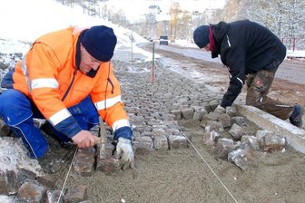Bodenfrost stoppt Straßenbauer auf dem Zöblitzer Bahnhofsberg - Die Straßenbauer Michael Weiß (l.) und Maximilian Martin waren am Montag am Bahnhofsberg bei Zöblitz mit Pflasterarbeiten beschäftigt. Im Hintergrund sind die Baumaschinen zu erkennen, mit den die Straße asphaltiert werden soll. Temperaturen im Frostbereich verhindern das zurzeit.