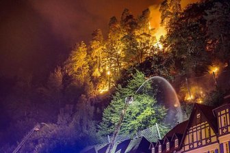 Brände im Elbsandsteingebirge - ganze Waldgebiete gesperrt - Flammen lodern direkt hinter Häusern im böhmischen Hrensko, während ein Feuerwehrmann zu löschen versucht. 