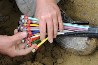 Breitbandnetz wird ausgebaut: Ab Montag Straßensperrungen in zwei Schwarzenberger Ortsteilen - Teil des Breitbandnetzes: Ein Mann fächert ein Glasfaserkabel mit farbigen Einzelsträngen auseinander.