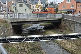 Brückenbau in Kirchbergs Zentrum startet nach Ostern: Was auf Kraftfahrer und Anlieger zukommt - Nach Ostern beginnen die Arbeiten zum Neubau der Brücke über den Rödelbach im Verlauf der Auerbacher Straße. Im Vordergrund das vorab errichtete Hilfsbauwerk, das für die Zeit der Bauarbeiten wichtige Kabeltrassen aufnimmt. Auch für Fußgänger wird eine Behelfsbrücke über den Rödelbach errichtet.