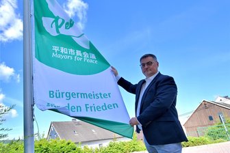 Bürgermeister im Erzgebirge zeigen Flagge für den Frieden - Volkmar Viehweg hisst die Friedensflagge. Die japanische Schrift erinnert daran, dass die Organisation 1982 auf Initiative des damaligen Bürgermeisters von Hiroshima, Takeshi Araki, gegründet wurde.