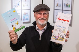 Cartoon-Ausstellung im Erzgebirge öffnet: „Ein bisschen Freude in unserer traurigen Zeit“ - Stephan Buße mit seiner Karikatur im Eulenspiegel-Postkartenkalender. Auch ein Kinderbüchlein hat er schon illustriert.